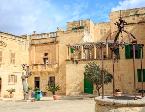 Mdina, Malta. Well at Misrah Mesquita square and traditional facade limestone buildings and blue sky background.